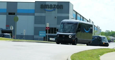 Amazon EV vans drive out of warehouse, made by Rivian, electric vehicles, Stock Footage 338195975
