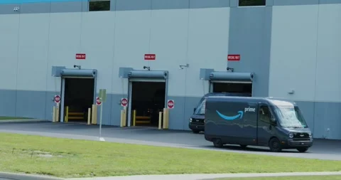 Amazon EV vans drive out of warehouse, made by Rivian, electric vehicles, Stock Footage 338196807