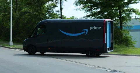 Amazon EV vans drive out of warehouse, made by Rivian, electric vehicles, Stock Footage 338196877