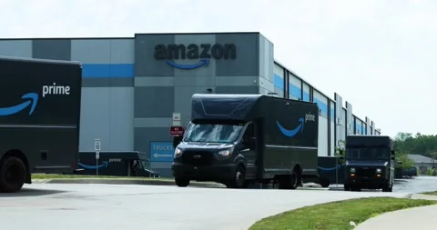 Amazon vans pull out of warehouse in a line with warehouse in background Stock Footage 338316223