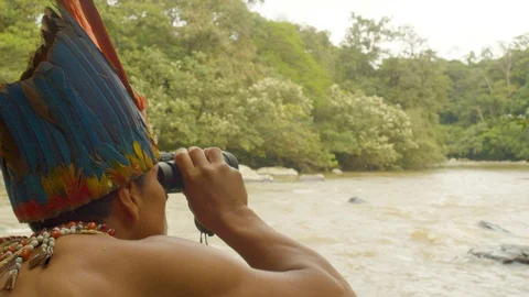 Amazonian indigenous warrior watching through a binocular a person in a kayak in Stock Footage 113512999