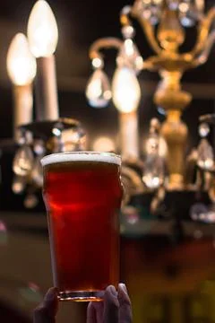 Amber craft beer held in front of an elegant crystal chandelier Photos