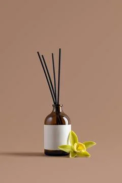 Amber glass reed diffuser with blank label and vanilla orchid flower on beige Stock Photos