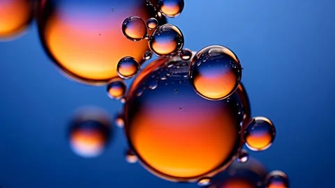 Amber oil spheres hover in clear liquid against cobalt Stock Footage 317215932