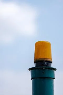 Amber Warning Beacon Mounted on Green Utility Pole Against Pale Cloudy Sky Stock-Fotos