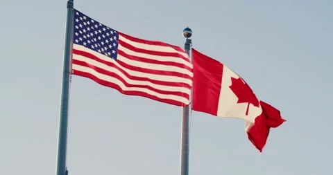 American and Canadian flags flutter in the wind against the sunset sky. Stock Footage 229878244