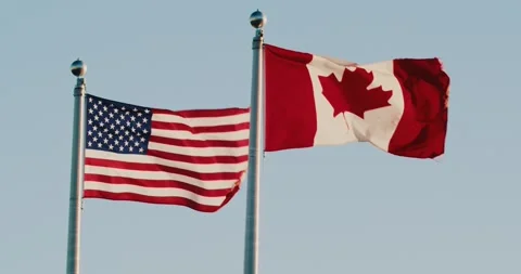 American and Canadian flags flutter in the wind against the sunset sky. Stock Footage 274148899
