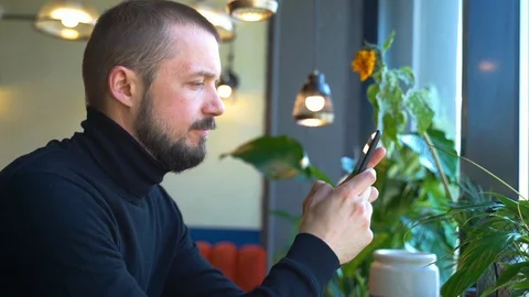 American bearded man is using phone and typing message at table in cafe spbd. Stock Footage 130170668