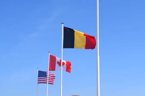 American, Canadian and Belgian flags with a blue sky in the background. Stock Photos