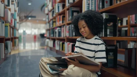 American elementary student sitting on floor in the library while reading a book Video stock 329401311