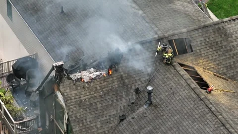American firefighter sith helmet and gas mask sitting on roof of burning house Stock Footage 313872707