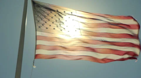 American flag, backlit by the sun, blows straight out on a windy day Stock Footage 36567295