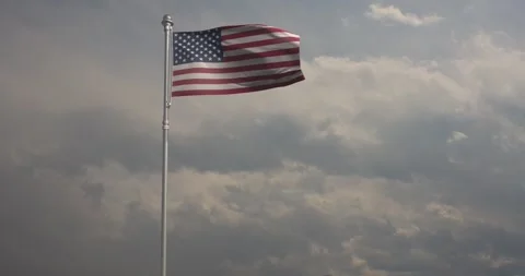 American flag billows energetically in the wind against a steely grey sky Stock Footage 240956211
