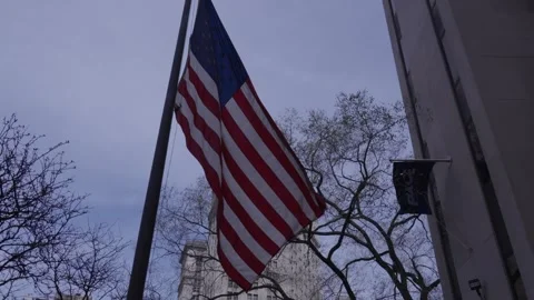 An American flag blows in the wind with a backdrop of a New York City court Stock Footage 241495611