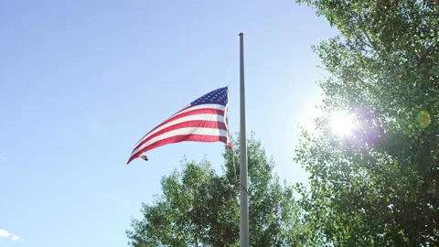 American flag dramatically waves at half mast with bright hopeful sun flaring Stock Footage 202223249