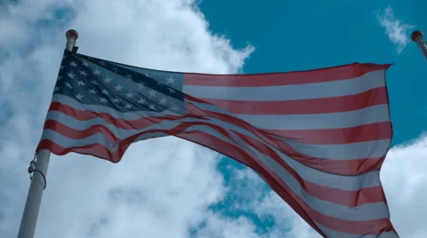 American flag on the flagpole waving in the wind against a blue sky with clouds Stock Footage 64723166