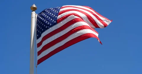 American Flag flaps in steady wind under blue sky Stock Footage 98933110