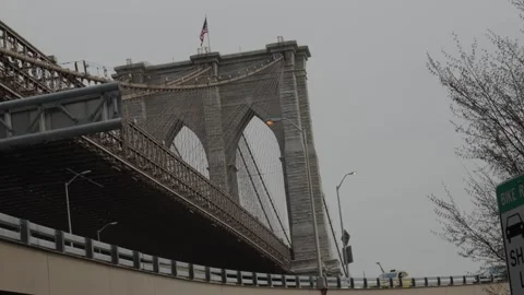 An American flag flies above the Brooklyn bridge as cars pass by on an overp Stock Footage 241495553