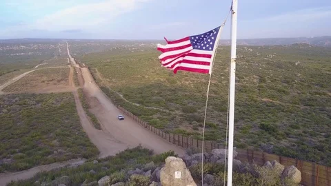 The American flag flies over the U.S. Mexico border wall in the California Stock Footage 79501523