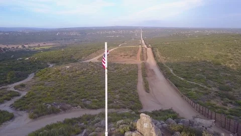 The American flag flies over the U.S. Mexico border wall in the California Stock Footage 79501543