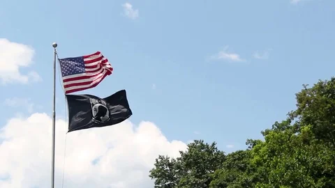 An American Flag flying with a Vietnam POW MIA Flag against blue sky Stock Footage