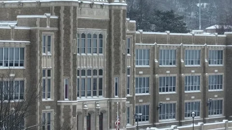 American flag in front of high school entrance during snow storm. Aerial Stock Footage 278076680