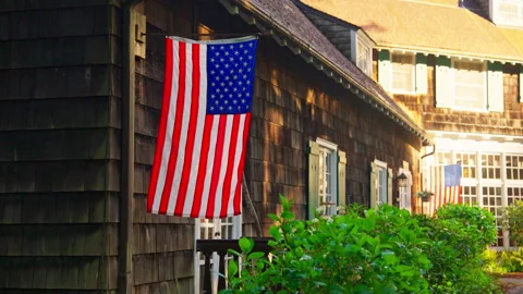 American flag hanging outside a rustic lodge, gently waving in the breeze Stock Footage 327459925