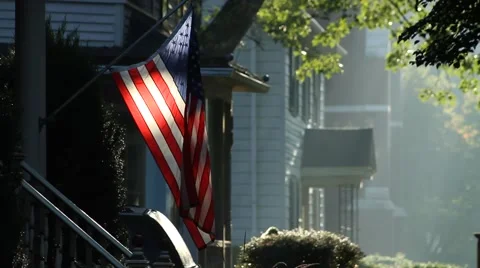 American Flag hangs limp outside house in a small town, hazy summermorning Stock Footage