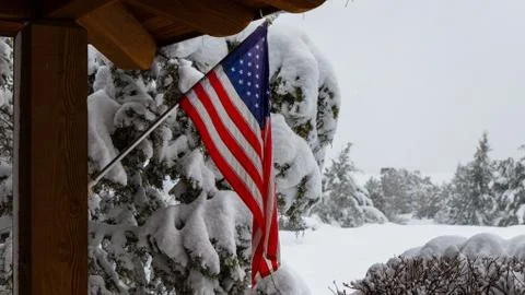 An American flag on a pole attached to a house or cabin surrounded by snow Stock Photos
