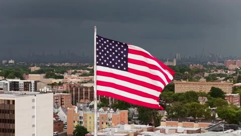 American flag waves against dark stormy clouds above dense rooftops in Orange Stock Footage 341842618