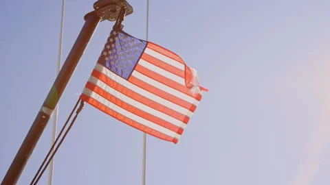 American flag waves in breeze, strong lens flare from bright sun, slow motion Stock Footage 242863113