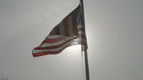 American flag waves in slow motion aganst a grey sunny sky Stock Footage 90819399