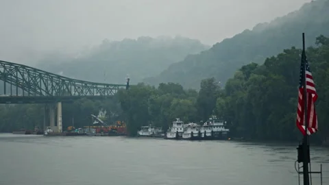 American flag waving on a boat navigating a foggy river with a bridge Video stock 334106311