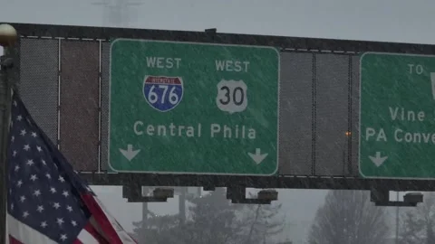 American flag waving during snowfall beside highway signs for Interstate 676 Stock Footage 331665086