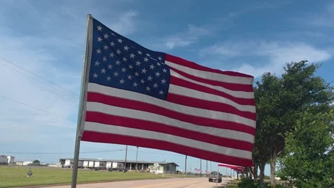American Flag Waving in Wind Beside Roadway Under Blue Sky Stock Footage 336872579