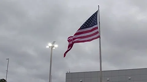 American Flag waving in the wind on a cloudy day with lights Stock Footage 149609698