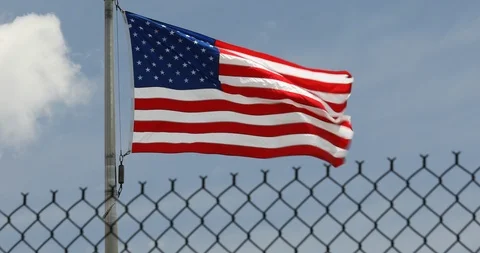 American flags blow in the wind behind a security fence Stock Footage 100853145