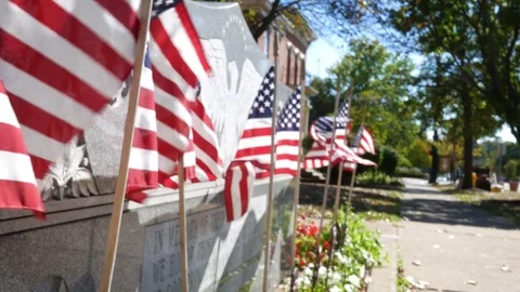 American flags blowing in small american town near war monument Stock Footage