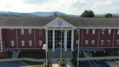 American flags fly before brick Amherst County Courthouse, white columns frame Stock Footage 345700424