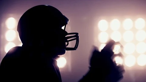 American football player putting on helmet against stadium illumination lights Stock Footage
