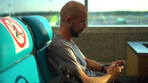 American guy hipster is using smartphone while waiting for flight at airport Stock Footage 143653894