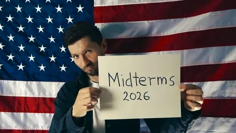 American Man Holding a Midterms 2026 Sign in Front of the United States Flag Stock Footage 335634492