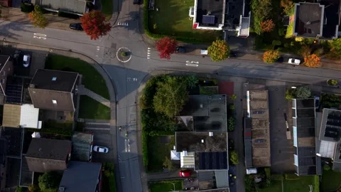 American roundabout intersection sits amid solar-paneled rooftops, parked cars Stock Footage 347700738