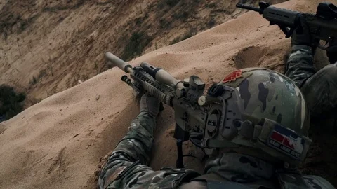 American soldiers in military gear lying on sand hill and shooting back view Stock Footage