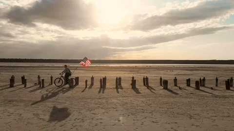 American trader on bicycle with a larger developing flag on a sunset background Stock Footage 122896169