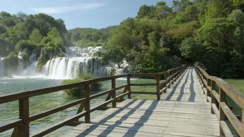 Amidst the lush trees and cascading waterfall, a wooden bridge guides travellers Stock Footage 259075090