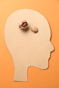 Amnesia problem. Paper cutout of human head and broken walnut on orange bac.. Stockfoto's