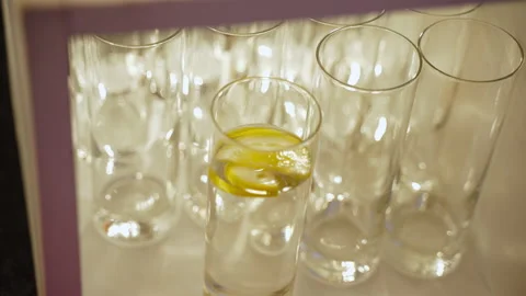 Among empty glasses is glass filled with water with slice of lemon on surface. Video stock 238779811