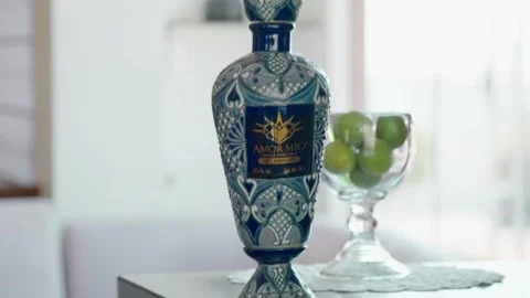 Amor Mio tequila bottle on a bar table with lemons and a luxury living room Stock Footage 306005552