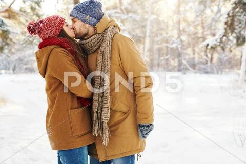 Amorous young couple in winterwear kissing outdoors Stock Photos